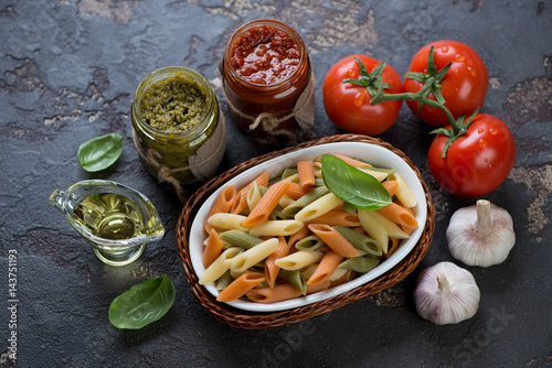 Penne of italian flag colors with red pesto and basil pesto and other cooking ingredients, horizontal shot