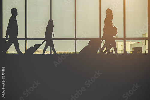 Travellers in airport walking to departures by escalator in front of window silhouette