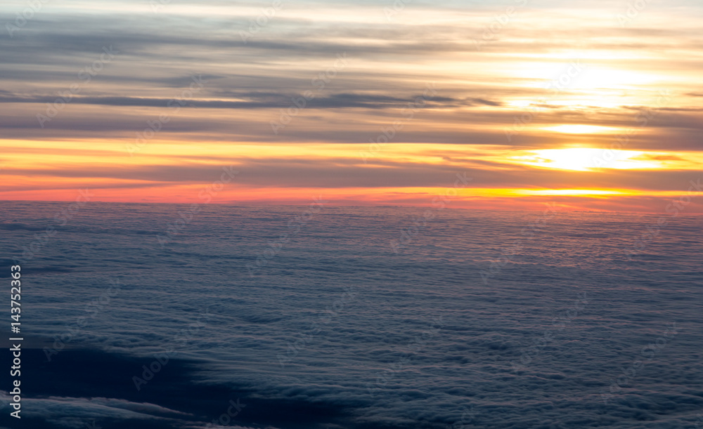 Sunset in sky view from plane flying over sea of clouds