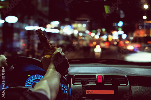 Man drink beer while driving at night in the city dangerously, left hand drive system