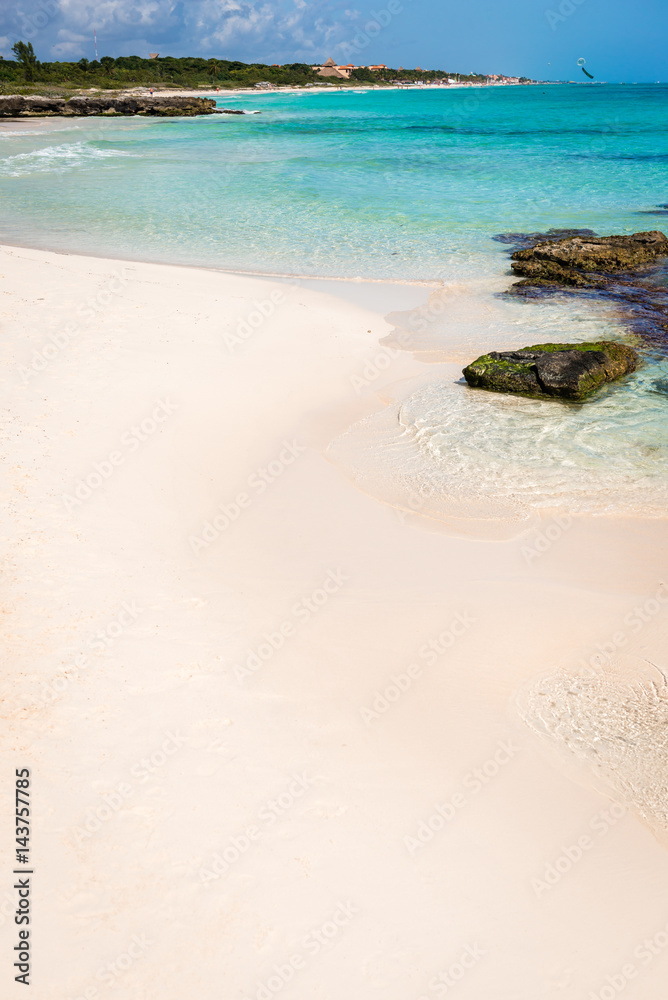 Wild tropical sandy beach with clear turquoise waters, soft waves, rocks and beautiful sky. Caribbean sea scenery in Playa Del Carmen, Riviera Maya, Mexico. Natural summer background with copy space.