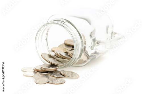 Coins spilling out of a glass jar and isolated on a white background.