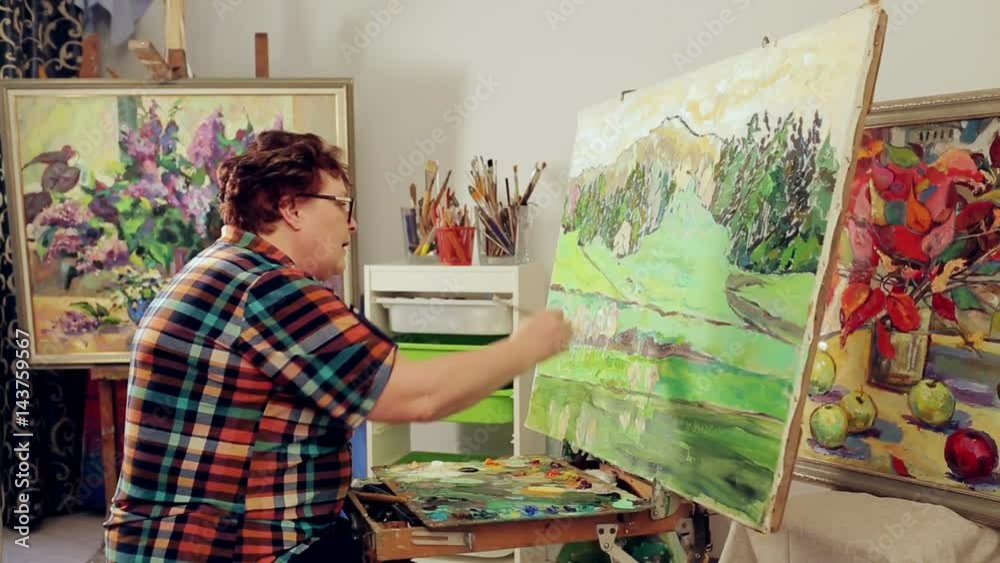 A woman paints a landscape with oil paints with a palette and brush. A woman paints a landscape with oil paints with a palette and brush.