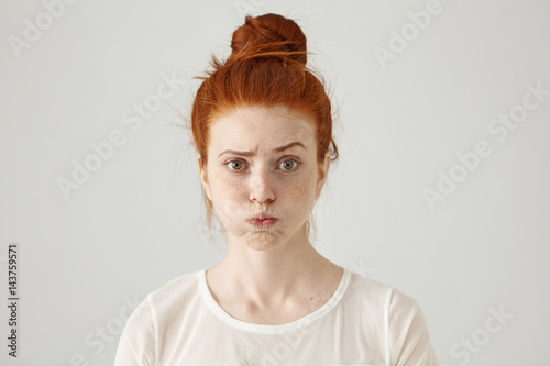Annoyed irritated young red-haired female with freckles blowing her cheeks, frowning, feeling frustrated with something. Human facial expressions, emotions and feelings. Fatigue or boredom concept