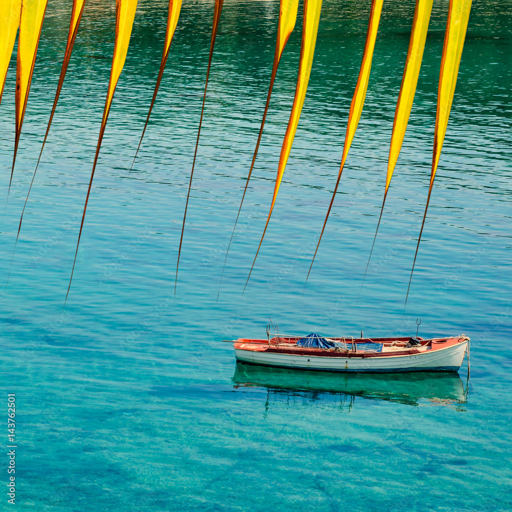 Yellow palm leaves, boat and clear sea water. Sea abstract background. Travel concept.