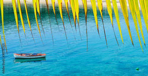 Obraz na płótnie Sandy beach with clear blue water, boat and palm leaf. Travel concept. w salonie