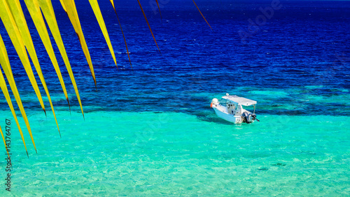 Tropical paradise - closeup of palm leaf and turquoise sea water with white boat. Summer background.