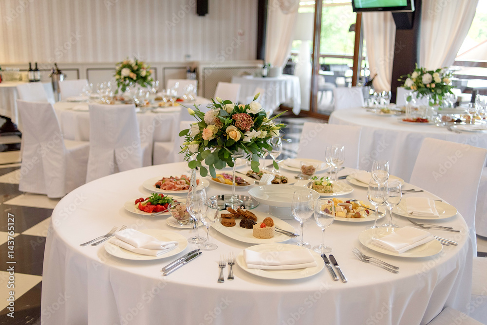 Beautiful bouquet in a glass vase on a dining table. White napkin on a white empty plate on a dining table. Table setting. Table served for wedding banquet, close up view