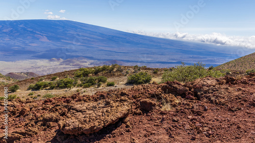 Red lava rocks on Mauna Kea, Mauna Loa in the background, colored blue from the atmosphere. photo