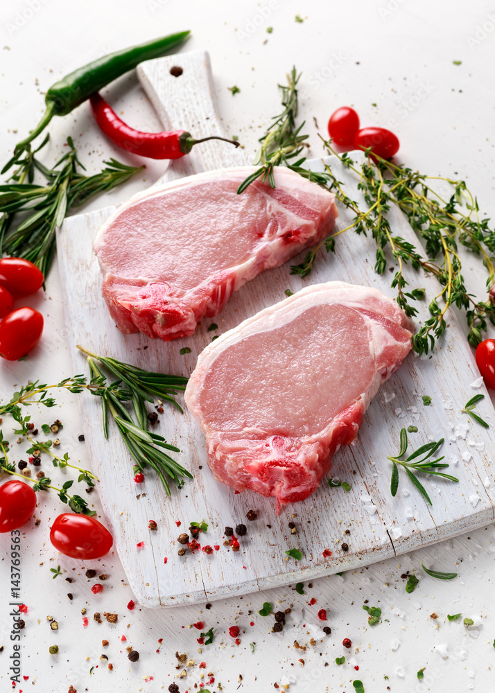 Raw Pork Loin chops on a cutting board with herbs, rosemary, thyme, chilli, salt, pepper on white cutting board. Raw Pork Loin chops on a cutting board with herbs, rosemary, thyme, chilli, salt, pepper on white cutting board.