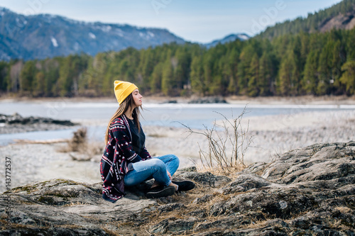 woman in sweater with tribal print sits on the shore of a mountain lake with closed eyes