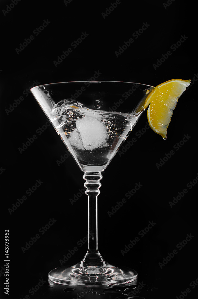 A glass with vermouth and ice cube on a black background