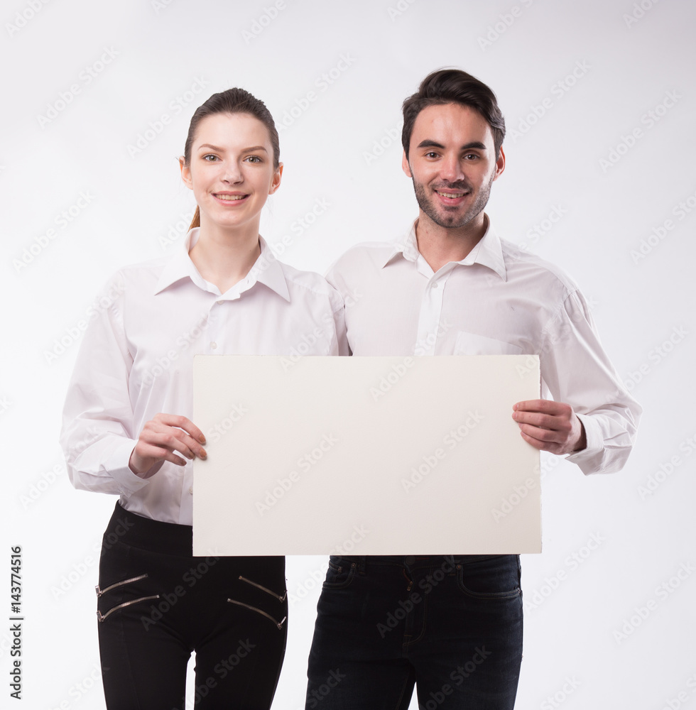 Young happy couple showing presentation pointing on placard over gray background Young happy couple showing presentation pointing on placard over gray background