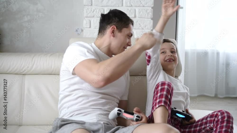 young father playing with his son in a video game and celebrating the victory. gives hi five young father playing with his son in a video game and celebrating the victory. gives hi five