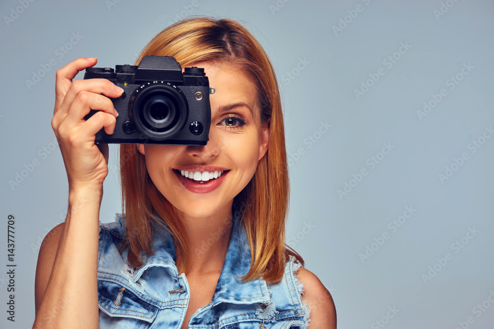 Smiling blond female holds compact digital photo camera.