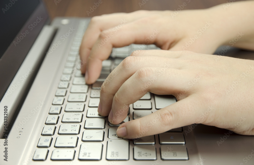 Closeup view of a hand with fingers typing on a keyboard Silver laptop lying on a wooden mat blurring Closeup view of a hand with fingers typing on a keyboard Silver laptop lying on a wooden mat blurring