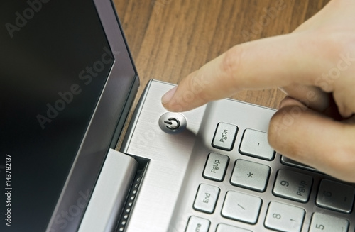 Closeup view of a hand with a finger, press the power button on metallic silver laptop keyboard, lying on a wooden mat blur