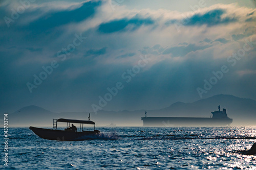 Big cargo ship and small fishing boat meet in rain cloud