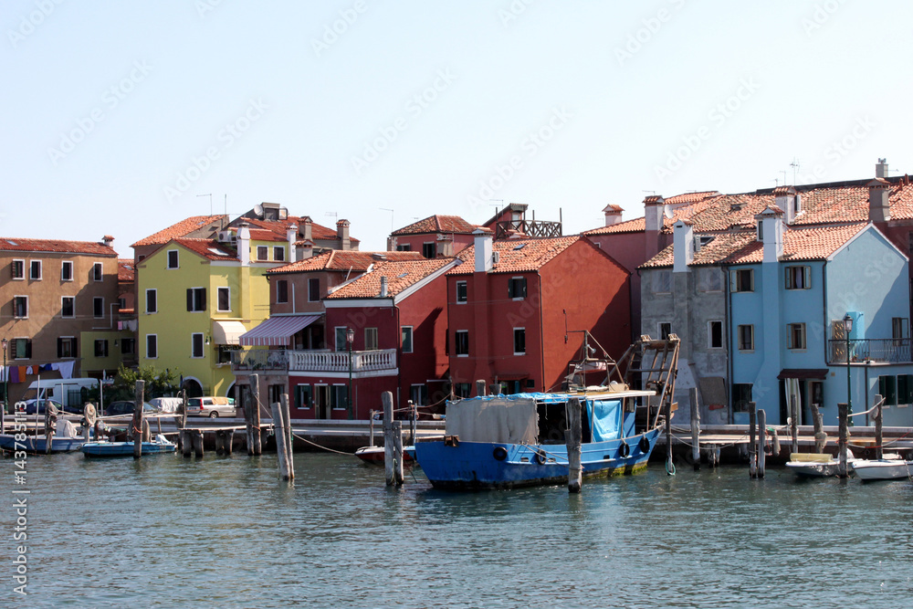 Italy. Venice. Colored red, yellow, blue houses near water and boats on blue sky background, horizontal view.