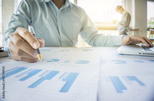 Handsome young businessman working with laptop while sitting on the desk in office and financial statistic graph photo