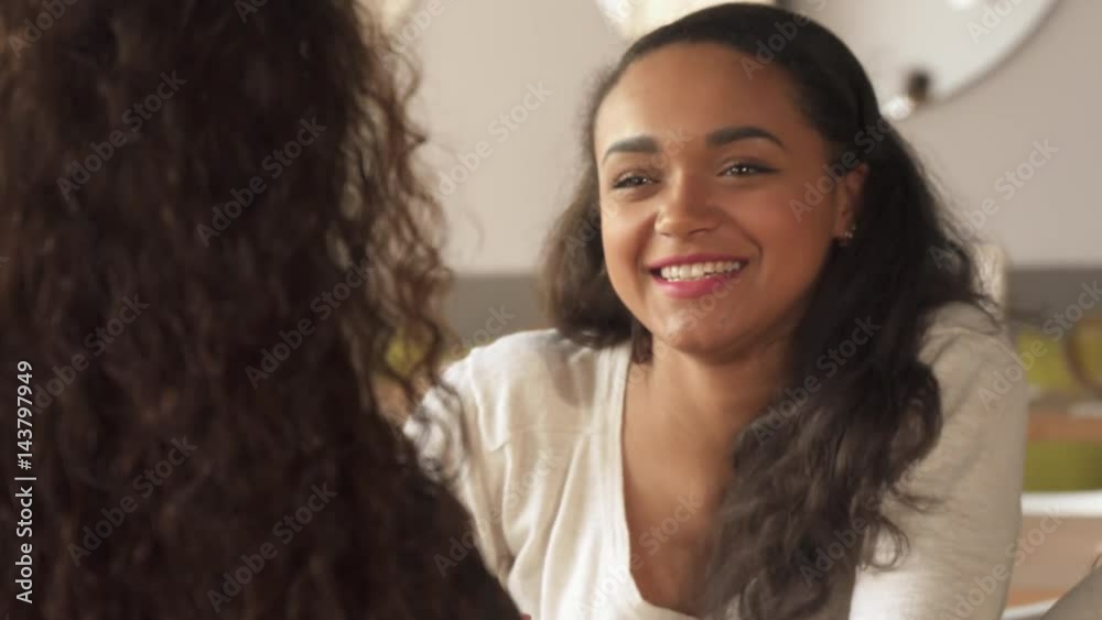Pretty african american girl asking some question to her female friend at the cafe. Cute brown haired woman taking a cup of coffee from the table. Close up of attractive young lady folding her palms Pretty african american girl asking some question to her female friend at the cafe. Cute brown haired woman taking a cup of coffee from the table. Close up of attractive young lady folding her palms
