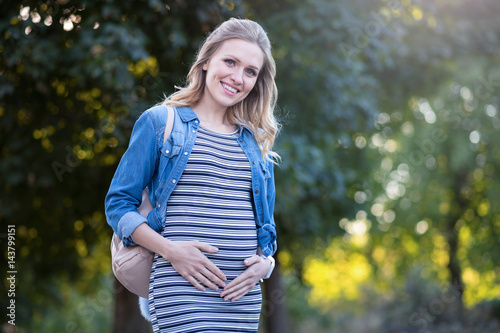 Peaceful young pregnant woman touching her belly outdoors