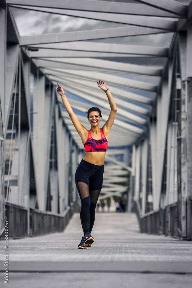 Portrait of young and sporty woman in sportswear walking along the bridge in Port Forum, Barcelona, Spain.