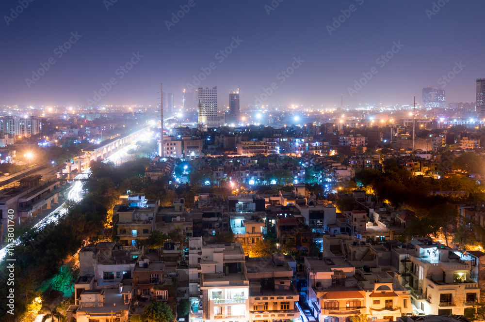 Noida cityscape at night with houses, office, skyscrapers, streets and metro rails visible. Lots of construction is visible as well showing the development