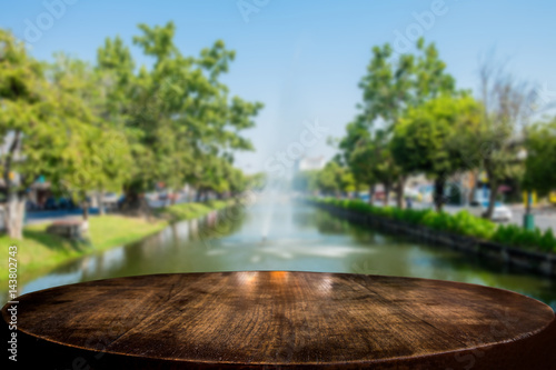 Selected focus empty brown wooden table and the fountain or canal blur background with bokeh image. for your photomontage or product display.