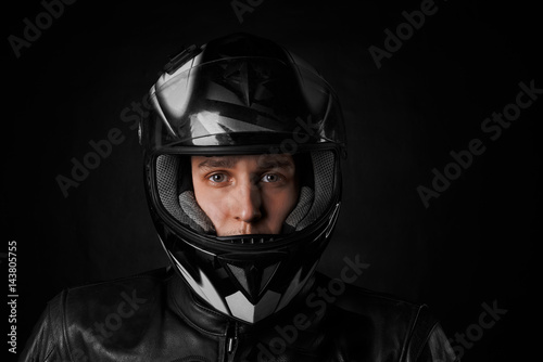 Close up portrait of young mustache biker in motorcycle black helmet and black leather jacket on black background. Moto life concept for advertising sport product. Seller of motorbikes.