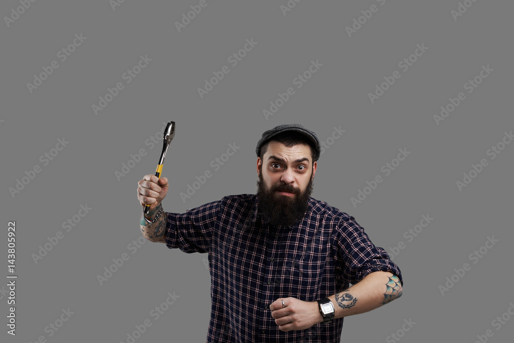 Dangerous beard hipster with tattooed hands and wrench. Crazy man run into the camera with aggressive face. Scare concept. Dangerous beard hipster with tattooed hands and wrench. Crazy man run into the camera with aggressive face. Scare concept.