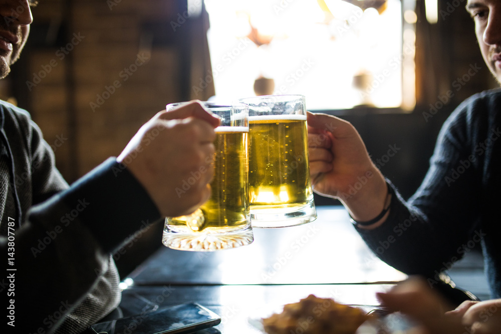 close up of male hands clinking beer glasses at bar or pub