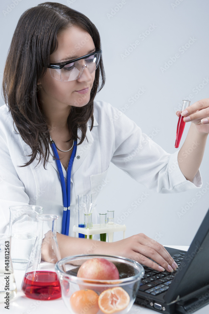 Researching Ideas and Concepts. Female Laboratory Assistant With Different Test Flasks Conducting Experiment in laboratory With Fruit Specimens. Researching Ideas and Concepts. Female Laboratory Assistant With Different Test Flasks Conducting Experiment in laboratory With Fruit Specimens.