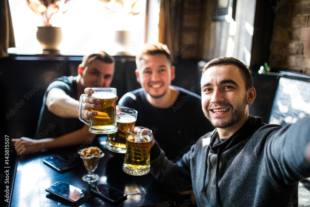 happy male friends drinking beer and taking selfie with smartphone at bar or pub