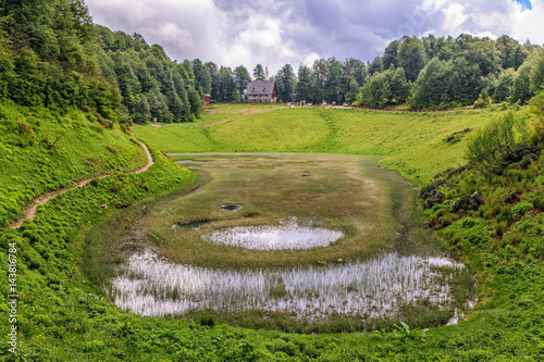 Mountain lake in karst cavity surrounded with green Caucasus mountain forest at summer. Beautiful scenic landscape