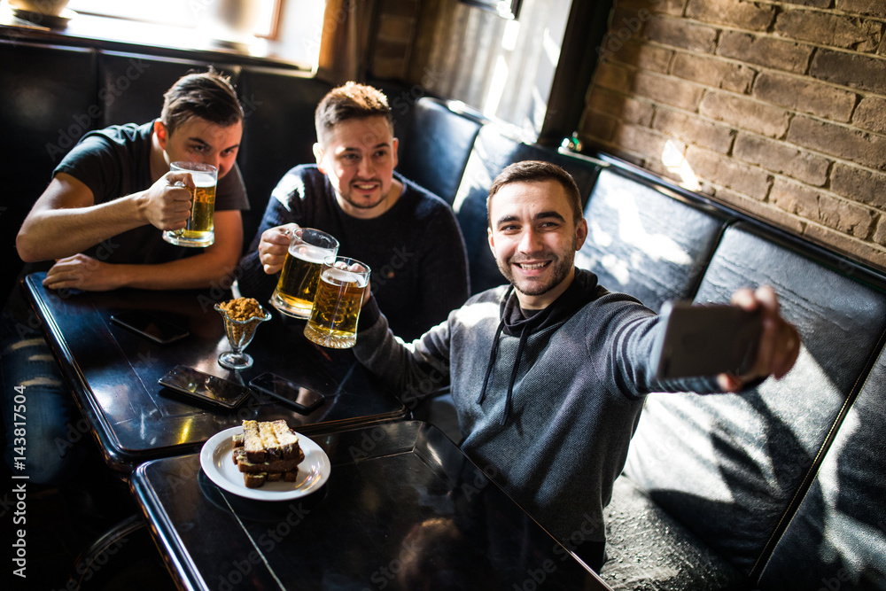 Handsome friends are drinking beer, doing selfie and smiling while resting in pub. Beer time.