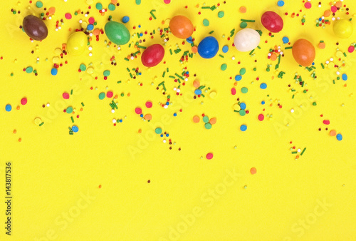 Easter chocolate egg with colorful explosion of candies and sweets on yellow colored background.