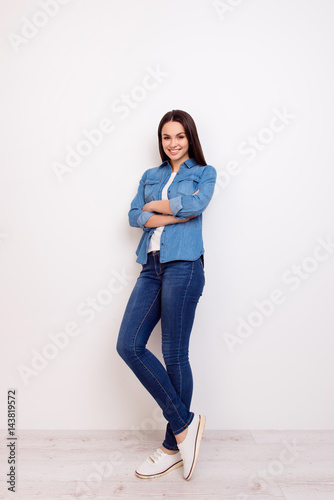 Full-length portrait of cute cheerful smiling young pretty woman in casual jeans clothes standing near white wall