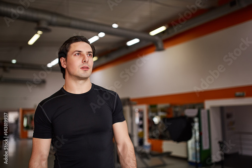 Lifestyle portrait of handsome muscular man in the black t-shirt standing in the sport gym.