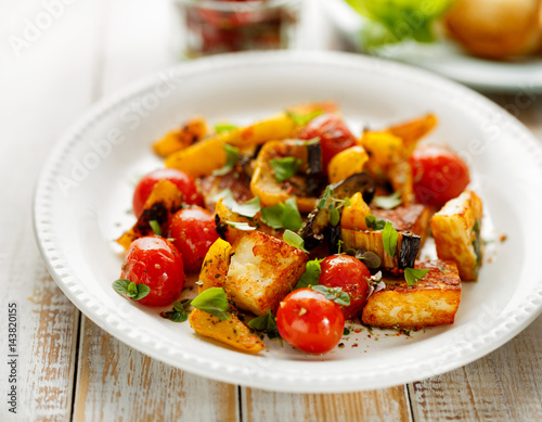 Salad with grilled halloumi cheese and vegetable with addition of aromatic herbs on a white plate