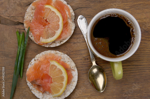 Breakfast: rice cookies with salmon and coffee cup. Snacks from rice cookies, salmon, lemon and coffee on wooden table top view.