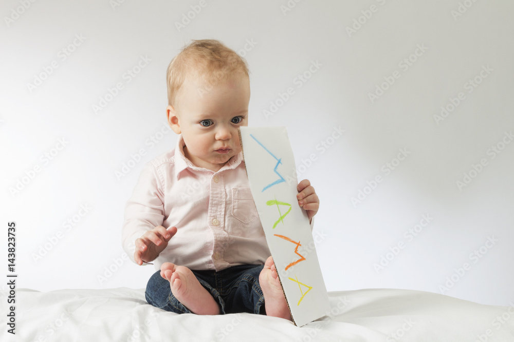Thougtful baby holding nameplate in his hands. Horizontal studio shot. Idea for postcards. Copy space. Mothers day Thougtful baby holding nameplate in his hands. Horizontal studio shot. Idea for postcards. Copy space. Mothers day