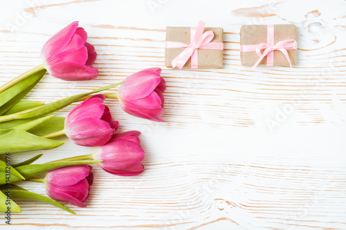 Букет розовых тюльпанов и упакованные подарки на белом деревянном фоне