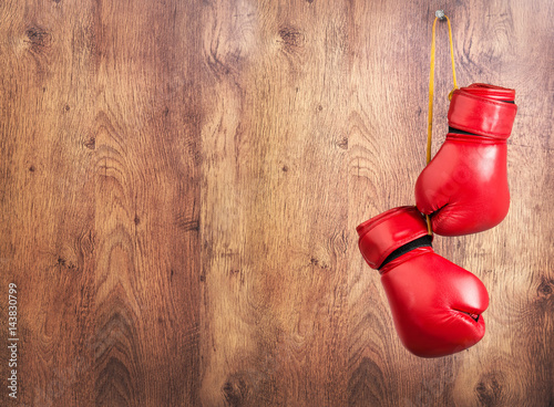 Pair of red leather boxing gloves hanging on a nail on a wooden wall.