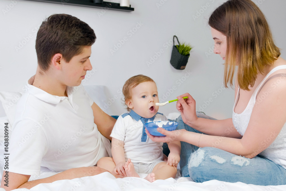 Young parents feed baby on a white background. Happy family. Young parents feed baby on a white background. Happy family.