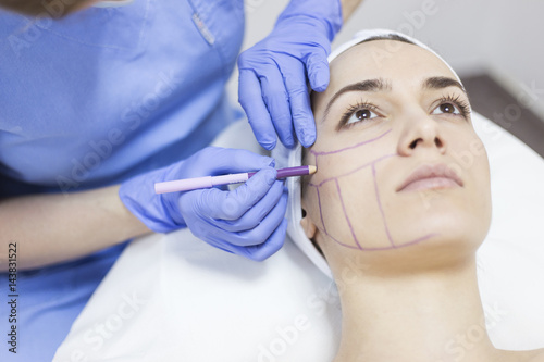 Beautician draw correction lines on woman face. Woman in beauty salon