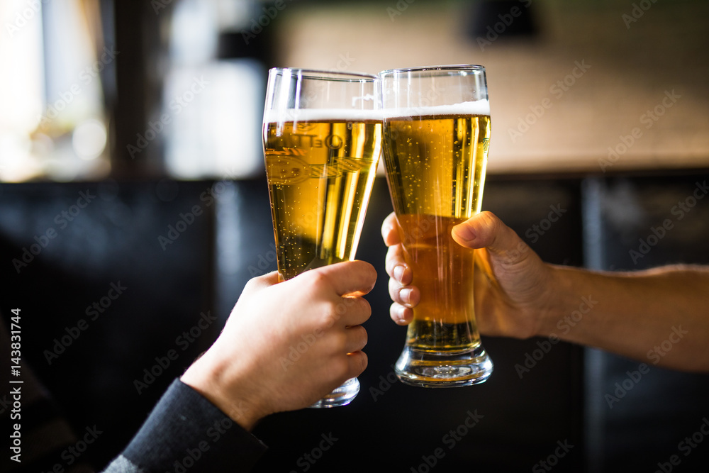 Men cheers with beer in glasses in pub. Close up.