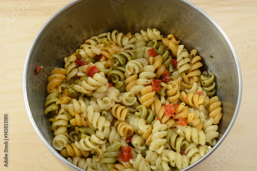 Vegetable rotini pasta salad with herb spice salad dressing in stainless steel mixing bowl
