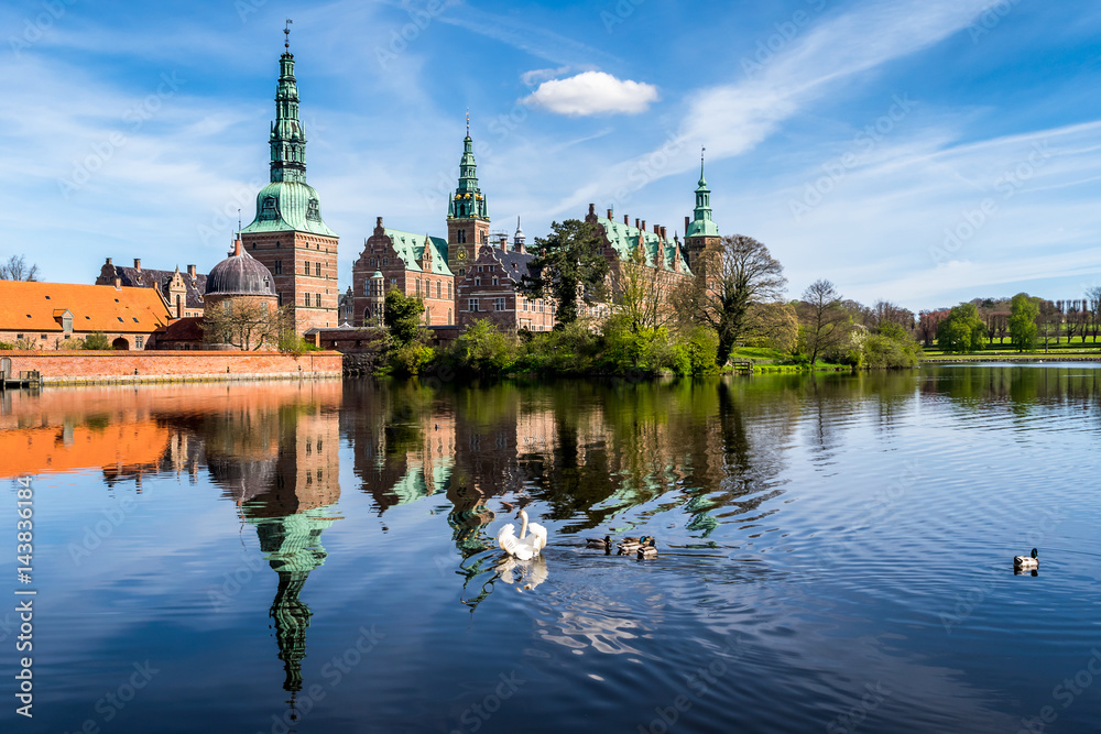 Morning sight of Frederiksborg Castle with the lake reflection, settled in a town Hilerod, north-west of Copenhagen, Denmark. A swan and several ducks swimming in the lake