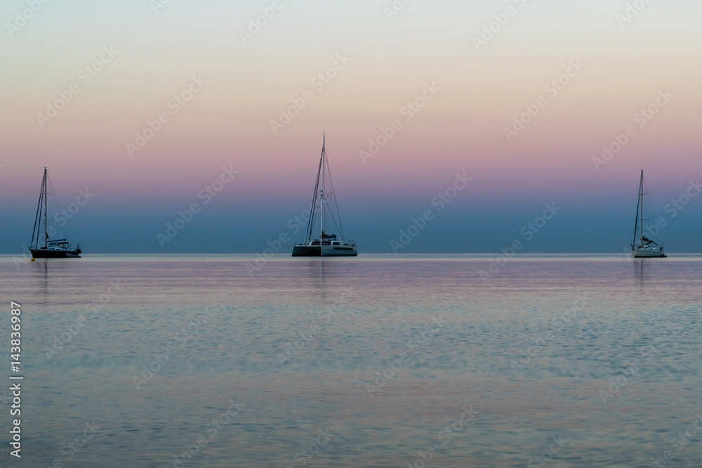 Three sail boats on the horizon at sunrise